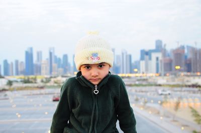 Portrait of boy standing in city against sky