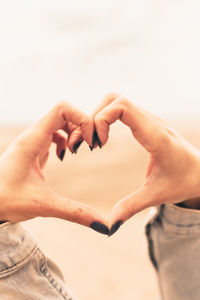 Close-up of hands making heart shape against sky