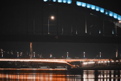 Illuminated bridge over river in city at night