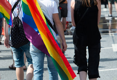 Midsection of man with rainbow flag walking on street