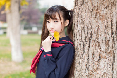 Portrait of beautiful young woman holding leaf standing outdoors