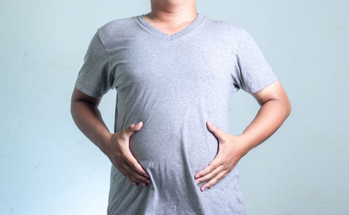 Midsection of man touching belly while standing against white background