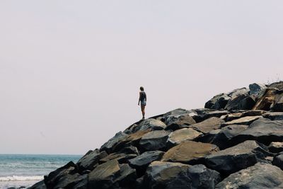 Woman standing on rocks by sea against clear sky