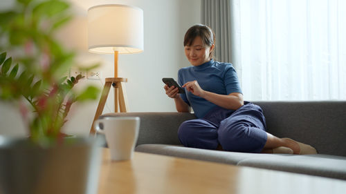 Young woman using mobile phone while sitting on sofa at home