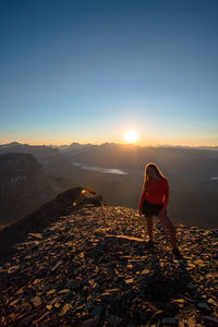 Rear view of man standing on mountain against sky during sunset