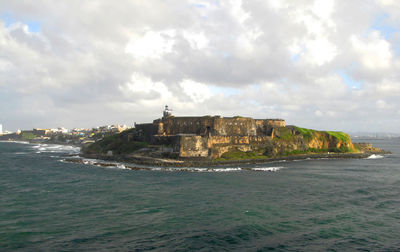 Buildings by sea against cloudy sky