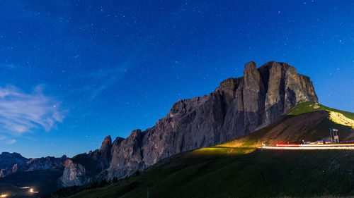 Scenic view of illuminated light trails on road by mountain against sky