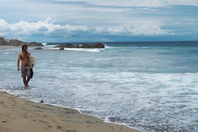 Rear view of shirtless man on beach against sky