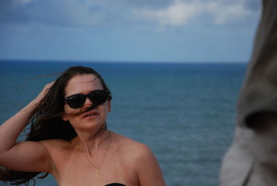 Young woman wearing sunglasses at beach against sky