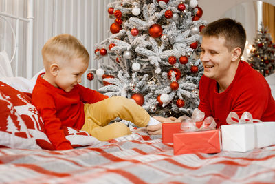 Young dad hold his son's leg and tickle it. christmas tree background