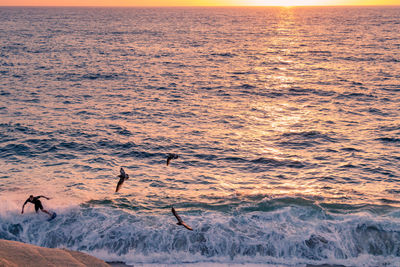 Silhouette people on sea against sky during sunset