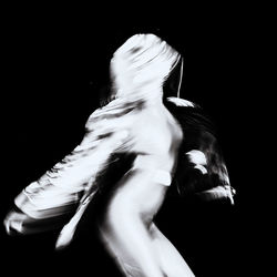 Rear view of woman dancing against black background