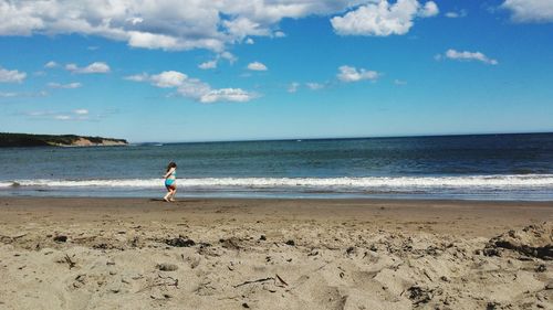 Full length of girl wearing bikini while walking on shore at beach against sky