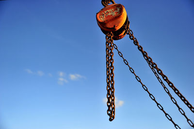 Low angle view of chain and pulley against sky on sunny day