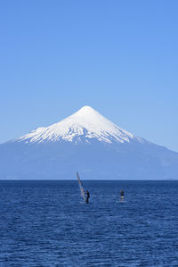 Scenic view of sea and mountains against clear blue sky