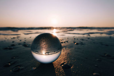 Close-up of crystal ball on beach against sky during sunset
