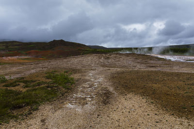 Steam rising from multicoloured geothermal field in geysir, iceland, during a cloudy day
