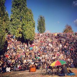 Large group of people sitting in park against blue sky