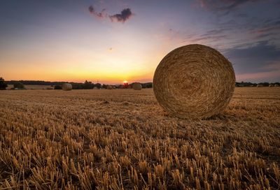 Hay bales on field against sky during sunset