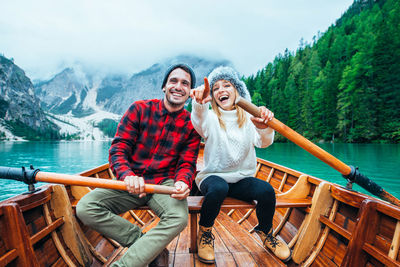 Full length of smiling young woman sitting on wood against mountain