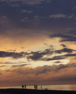 Silhouette people on beach against sky during sunset