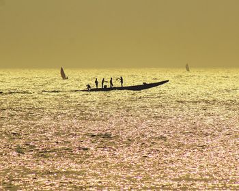 Silhouette people on boat in sea against sky during sunset