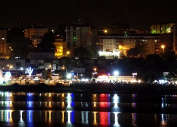 Illuminated buildings by sea against sky at night