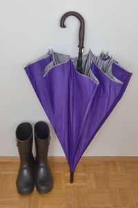 High angle view of purple umbrella with rubber boots on hardwood floor