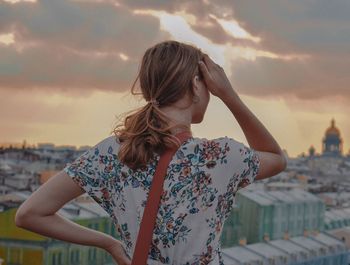 Senior woman standing by cityscape against sky during sunset