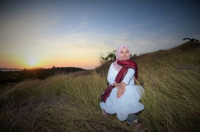 Portrait of woman sitting on field against sky during sunset