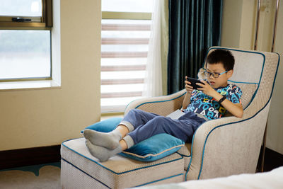 Boy using phone while sitting on chair at home