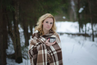 Portrait of young woman covering face on snow covered landscape