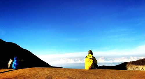 People sitting on top of mountain against blue sky