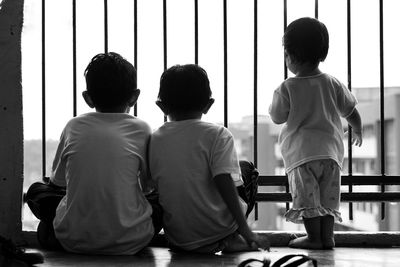 Rear view of siblings sitting on window sill