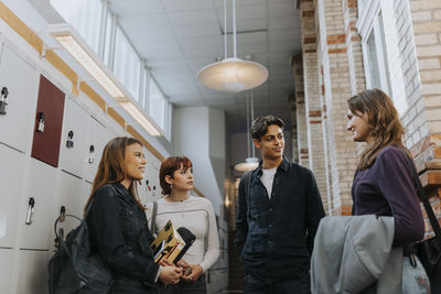 Male and female students talking while standing in school corridor