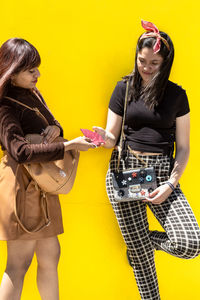 Woman giving mask to girl against yellow background