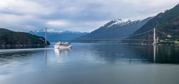 Cruise ship sailing on river near bridge by snow covered mountains against sky