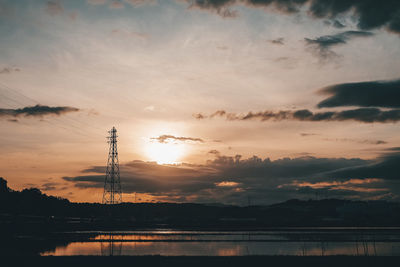 Silhouette electricity pylon by lake against sky during sunset
