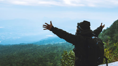 Man with arms outstretched while standing on mountain against sky