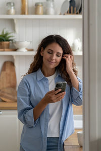 Portrait of young woman using mobile phone while sitting at home