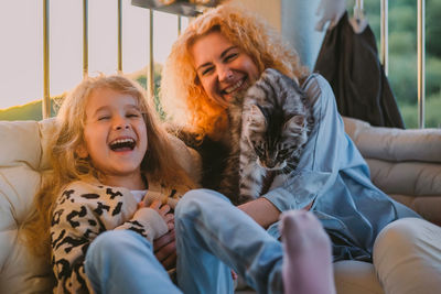 Happy child with smile plays on summer at home with mom, cat at sunset. cat, dog, pets family member