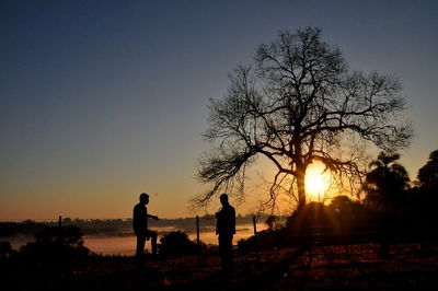 Silhouette man and bare trees against sky during sunset