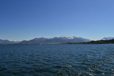 Scenic view of sea and mountains against clear blue sky