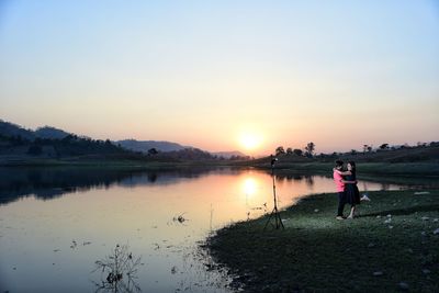 Man standing on shore against sky during sunset