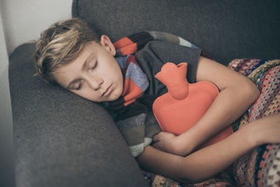 Boy with hot water bottle sleeping on sofa at home