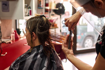 A close-up of a hairdresser cutting client's hair with a face shield