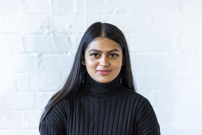 Smiling young businesswoman in front of white wall