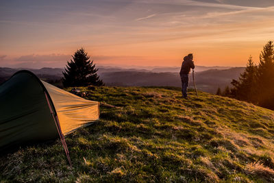 Rear view of man standing on mountain against sky during sunset
