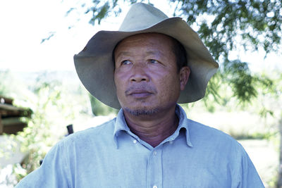 An elderly man standing in a cowboy hat native to thailand taking a close-up of his face.
