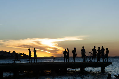 Silhouette of young people jumping from the crush bridge at the yellow sunset .